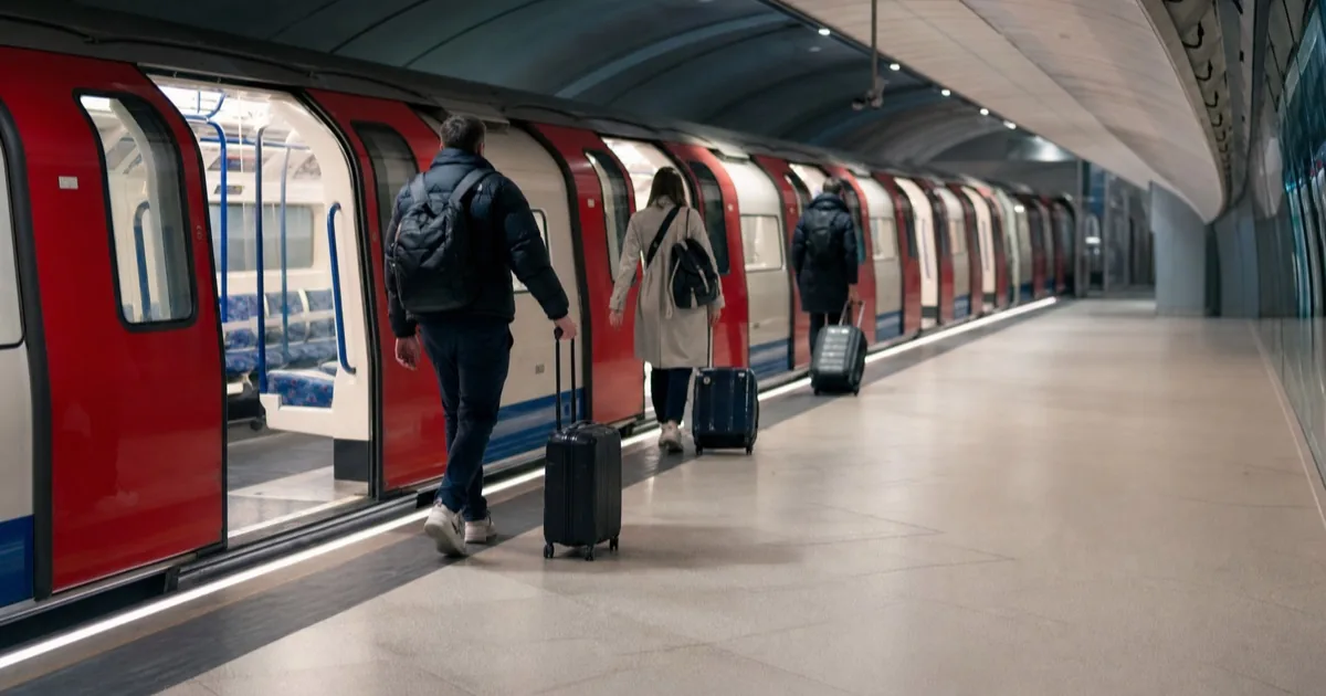A London Underground Piccadilly line train at the Heathrow Terminal 5 platform with travellers and suitcases